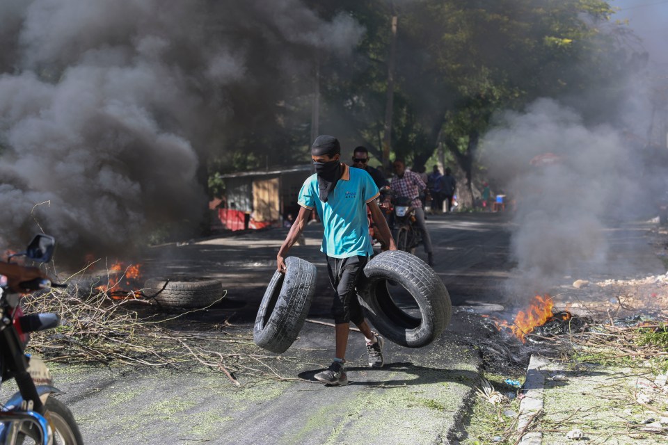 A resident carrying tires across a road to create a burning barricade to stop Barbecue's men entering