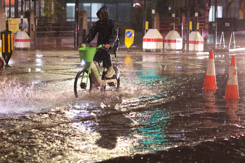 A cyclist navigates deep surface water on the Euston Road in Central London during heavy rain